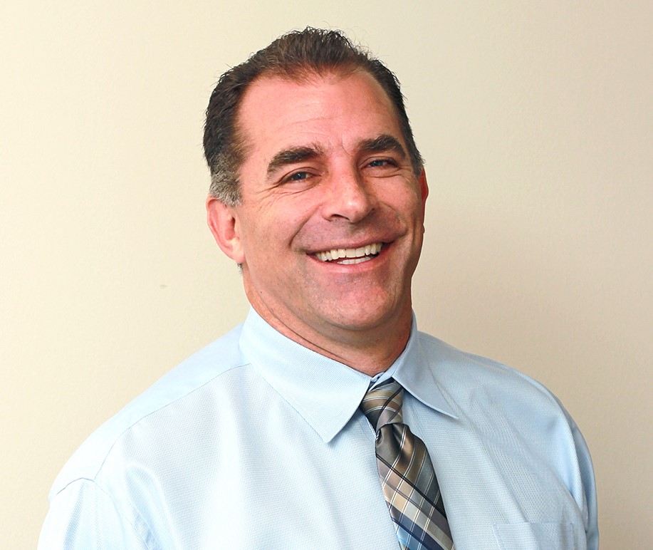 A man in a blue shirt and tie smiling for the camera.